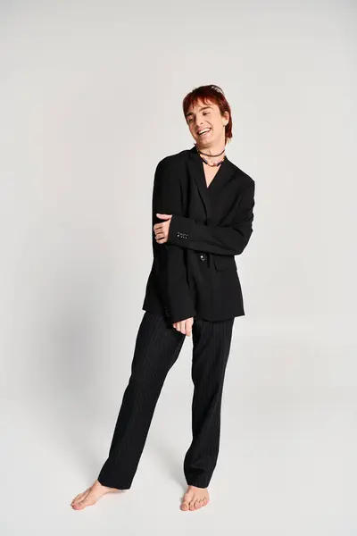 stock image A sophisticated man in a black suit strikes a captivating pose with confidence in a studio setting against a grey background.