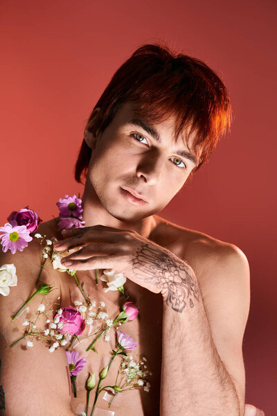 A young man strikes a pose shirtless with vibrant flowers adorning his chest, set against studio backdrop.