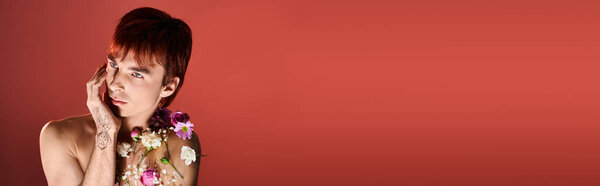 A young man adorned with blooming flowers in a studio against background.