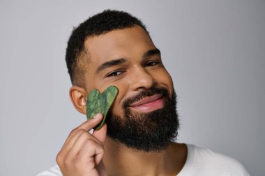 African american young man holds gua sha for skincare routine. clipart