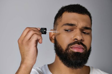 African american handsome young man with a beard holding a bottle of serum. clipart