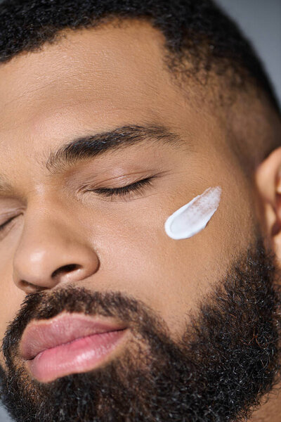 Close-up of a young man with a beard applying cream.