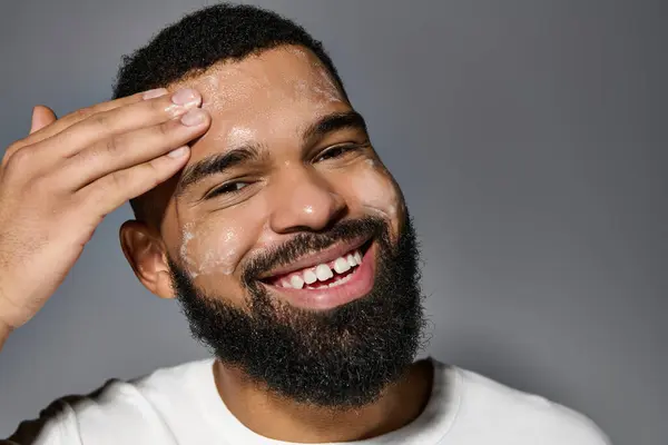 stock image Handsome man with beard in white t-shirt, focusing on skincare routine.