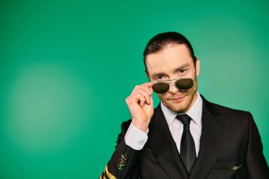 Siyah üniformalı şık bir erkek pilot yeşil zeminde poz veriyor..
