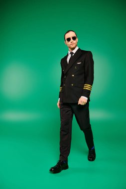 Siyah takım elbiseli ve güneş gözlüklü şık bir pilot parlak yeşil bir arka plana karşı güvenle duruyor..