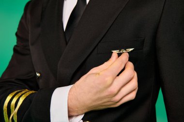 Sivri takım elbiseli ve kravatlı bir pilot yeşil bir zemine karşı güvenle duruyor..