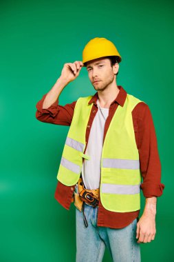 Güvenlik yeleği ve kasketli bir adam yeşil arka planda aletlerle güvenle poz veriyor..