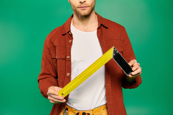 A handsome male worker in uniform holds a measuring tape on a green backdrop.
