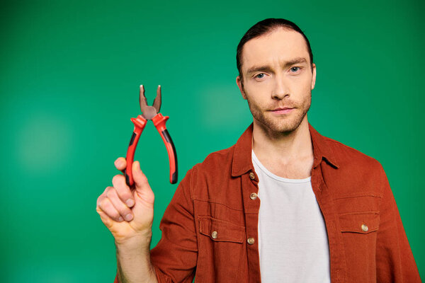 Handsome worker holding scissors in hand on green backdrop.