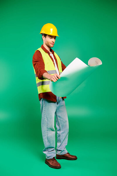 A handsome male worker in a hard hat holds a piece of paper against a green backdrop.