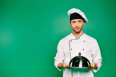 A handsome male chef in a white uniform proudly holds a platter on a green backdrop. clipart