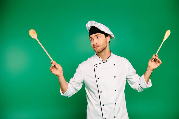 Handsome chef in white uniform holding two wooden spoons.