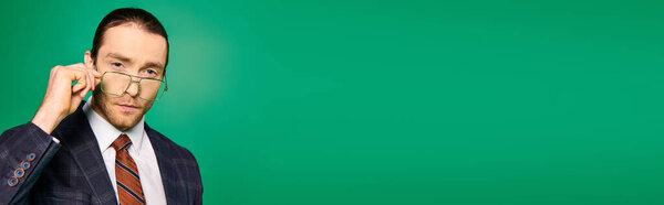 Handsome businessman in a chic suit and tie holding a pair of glasses.