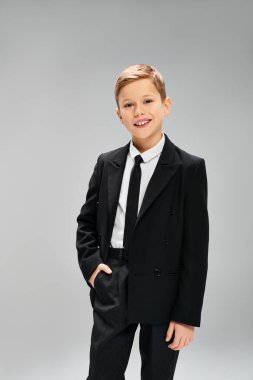 Stylish preadolescent boy in a suit and tie against gray backdrop. clipart