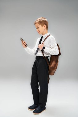 A young boy dressed in a white shirt and tie, holding a cell phone. clipart