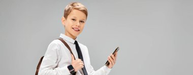 Preadolescent boy in white shirt and tie holding a cell phone, portraying a business concept. clipart