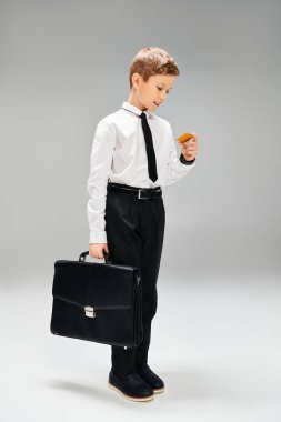 Takım elbiseli ve kravatlı genç bir çocuk, elinde bir evrak çantası tutuyor..