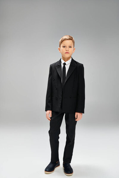 Предрожденный мальчик в остром костюме и галстуке на сером фоне.