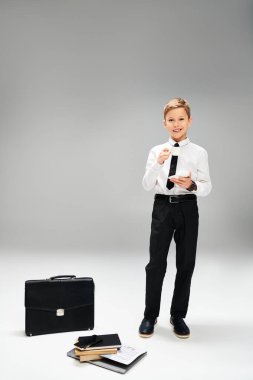 Zarif giyinmiş, bir bavulun yanında duran, bir iş konseptini somutlaştıran ergenlik öncesi bir çocuk..