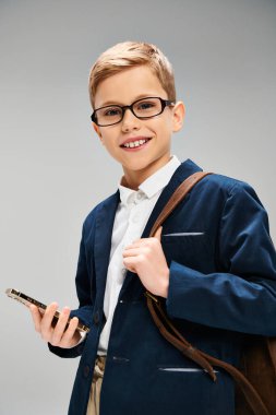 Gözlüklü, cep telefonu tutan genç bir çocuk. Gri arkaplan üzerine iş konsepti.