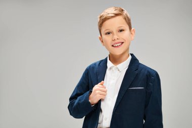 A little preadolescent boy in a blue jacket and white shirt, exuding elegance and sophistication on a gray backdrop. clipart