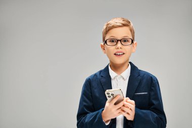 Gri arka planda cep telefonu kullanan gözlüklü, zarif ergen çocuk..