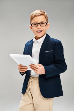 Takım elbiseli ve gözlüklü ergen bir çocuk kendine güvenen bir tablet tutuyor..
