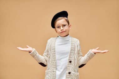 A cute preadolescent boy in glasses and a hat, dressed as a film director on a beige backdrop. clipart