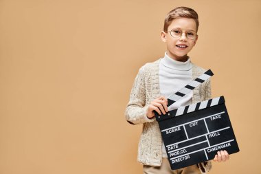 Film yönetmeni kılığına girmiş genç bir çocuk, elinde bir film tahtası tutuyor..