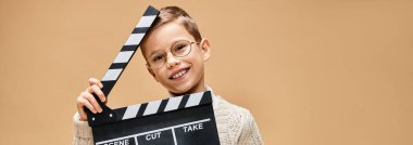 Preadolescent boy mimics a film director with clapper board. clipart