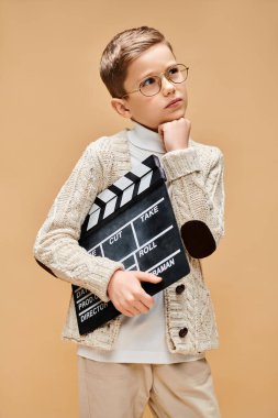 Gözlüklü genç bej arka planda film panosu tutuyor..