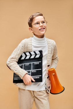 Film yönetmeni gibi giyinmiş genç bir çocuk elinde bir alkış tutuyor..