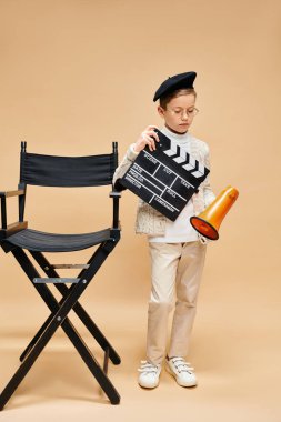 Sandalyenin yanında film şaplağı tutan tatlı bir ergen çocuk..