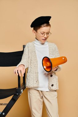 Film yönetmeni gibi giyinmiş genç bir çocuk elinde turuncu ve siyah bir megafon tutuyor..