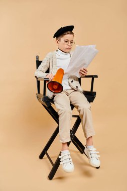 Film yönetmeni gibi giyinmiş ergenlik öncesi bir çocuk bir sandalyeye oturup gazete okuyor..