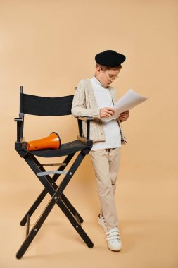 Preadolescent boy dressed as film director reading a paper in folding chair. clipart