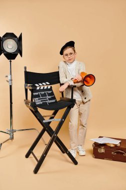 A little boy stands proudly next to a directors chair. clipart
