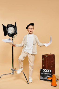 Preadolescent boy dressed as a film director on beige backdrop. clipart
