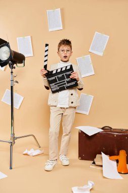 Film yönetmeni kostümü giymiş genç bir çocuk kameranın önünde tahtasını tutuyor..