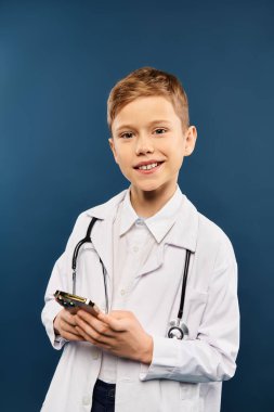 Preadolescent boy in doctors coat holding cell phone. clipart