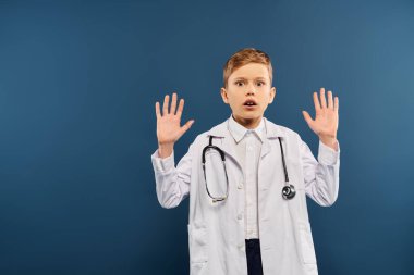 A preadolescent boy in a white lab coat, hands raised, on a blue backdrop. clipart