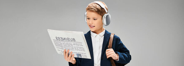Мальчик в элегантной одежде, в наушниках, погруженный в чтение газет.