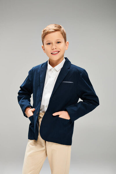 A young boy dressed in a stylish blue jacket and tan pants, exuding elegance on a gray backdrop.