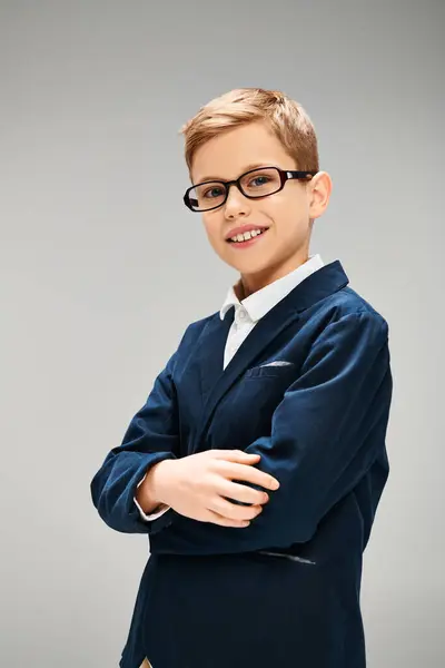 stock image A preadolescent boy in elegant attire, wearing glasses, strikes a confident pose against a gray backdrop.