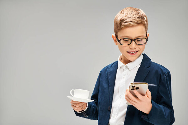 Предприимчивый мальчик в элегантном наряде, держа в руках чашку и мобильный телефон.