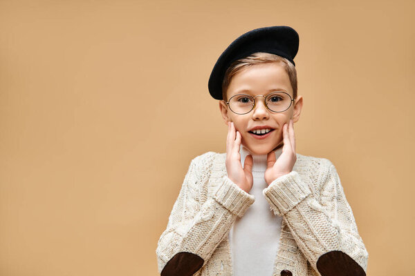 Young boy in glasses and hat, dressed as a film director, against beige backdrop.