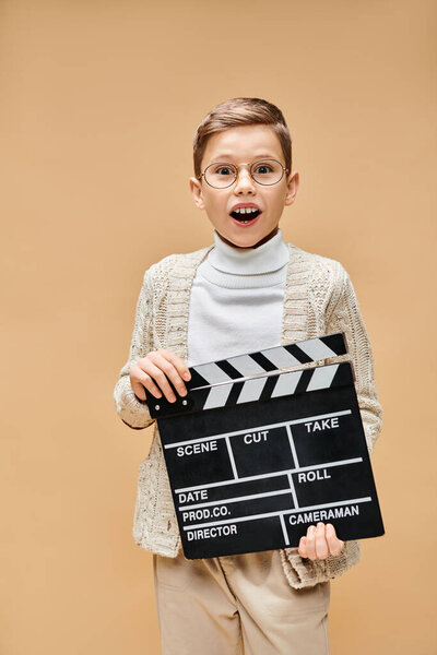 A young boy disguised as a film director holds a clap board in front of his face.