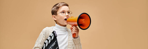 A preadolescent boy dressed as a film director, holding a red and orange megaphone.