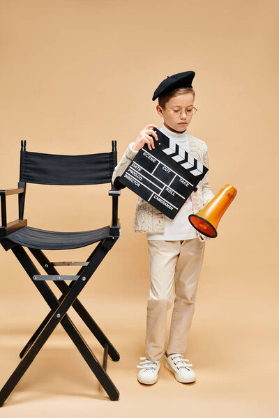 A cute preadolescent boy holding a movie clapper near a chair.