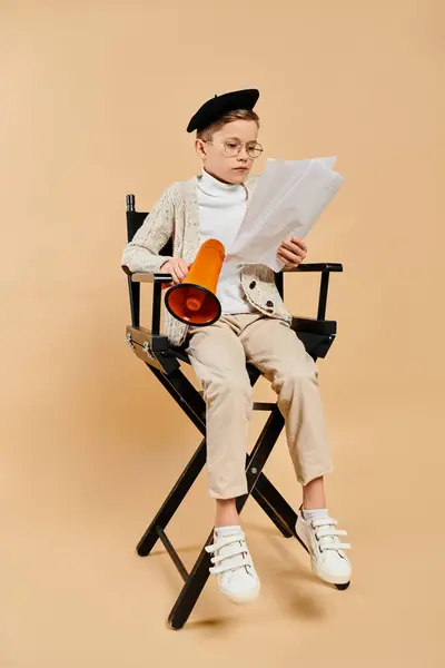 映画監督として服を着た若い少年は 紙を読む椅子に座る — ストック写真